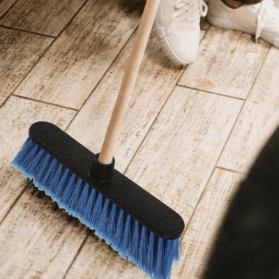 il nettoie sol en bois avec balai terrasse