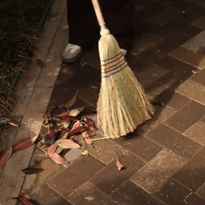 homme balaye feuille sur sol en carrelage extérieur avec balai en paille
