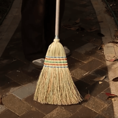 homme balaye sol en carrelage extérieur avec balai en paille
